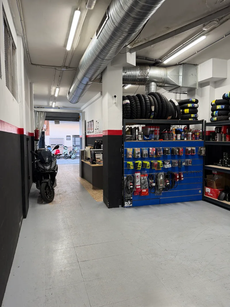 Interior del taller visto hacia la puerta de la calle, con una moto aparcada y el panel de recambios